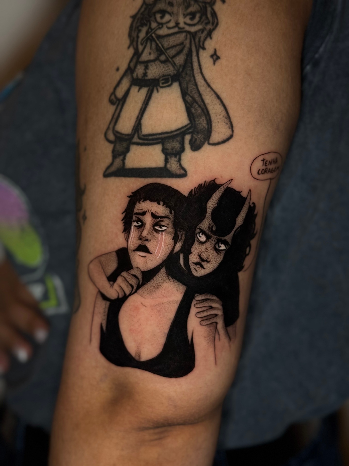 Illustrative black and grey tattoo of two figures embracing on the arm